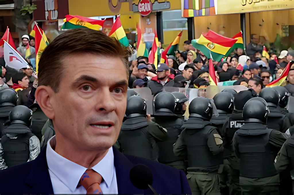 Hombre habla ante micrófono con fondo de protesta boliviana y policía.