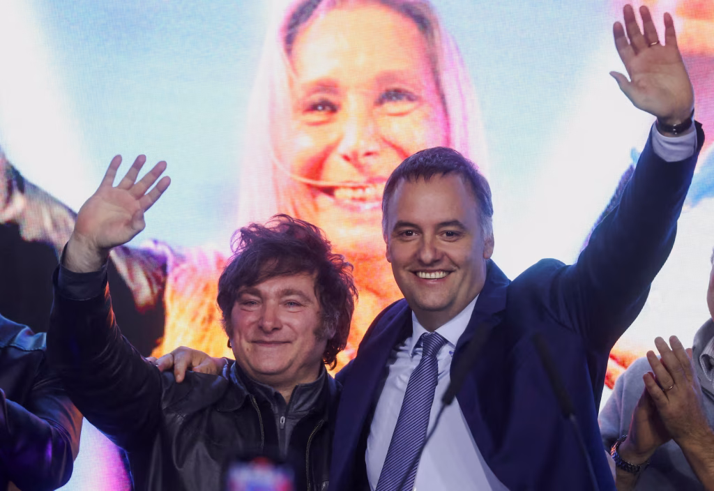 Milei Adorni sonriendo y saludando en un evento político.