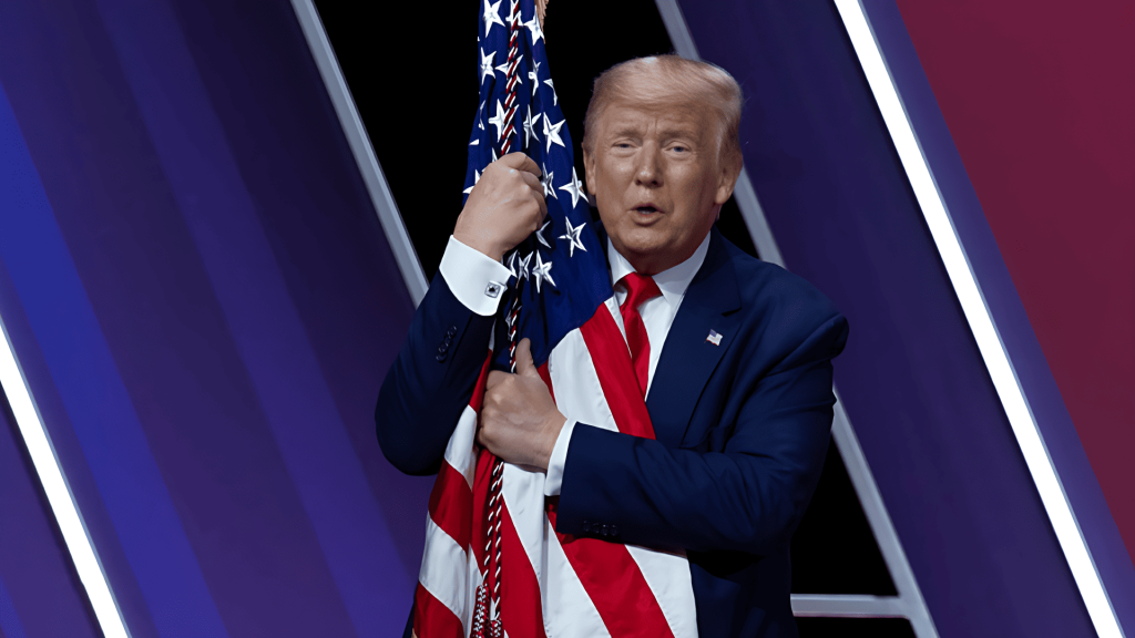 Donald Trump sosteniendo la bandera de Estados Unidos, hablando.