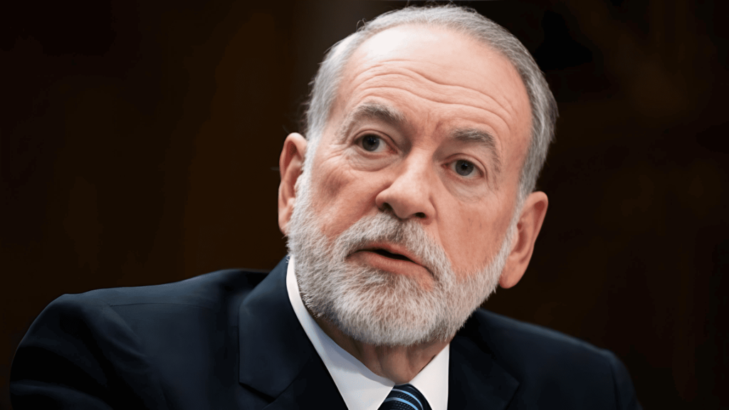 Hombre mayor con barba gris y traje, expresión seria.