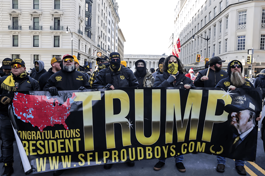 Manifestación de hombres sosteniendo pancarta "TRUMP" y símbolos Proud Boys.