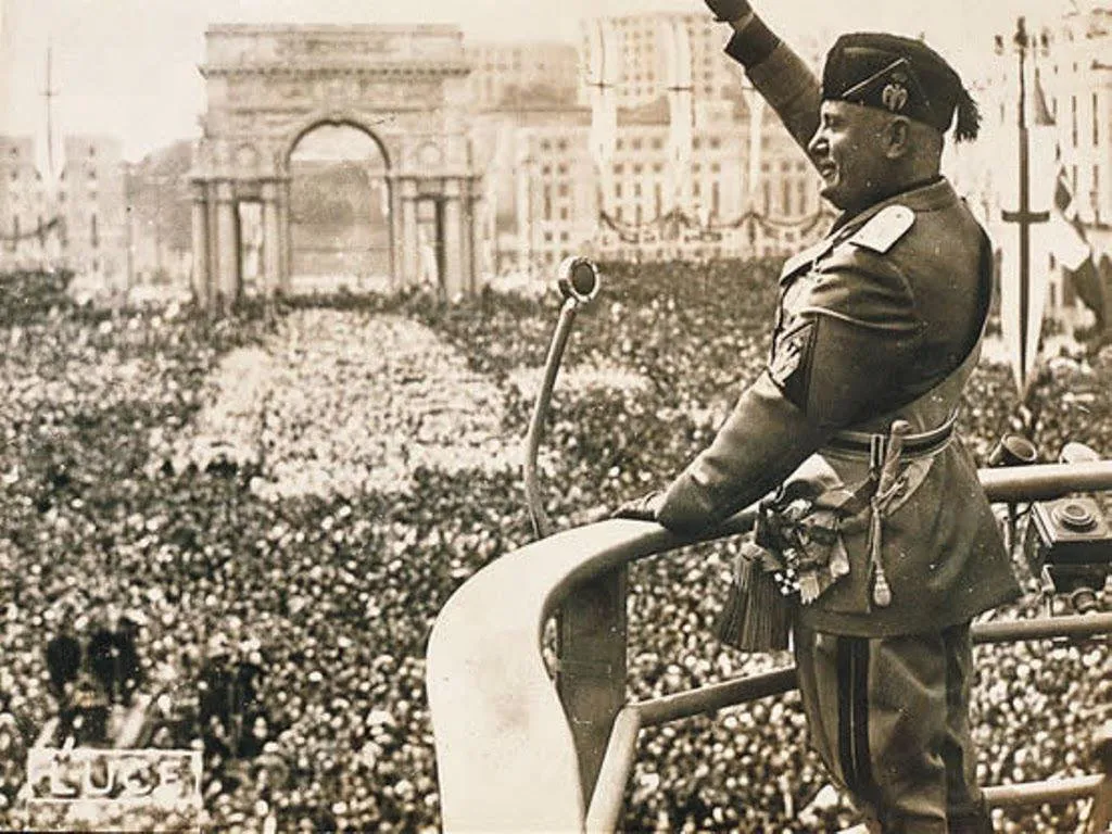 Mussolini saludando a la multitud frente a un arco triunfal histórico.