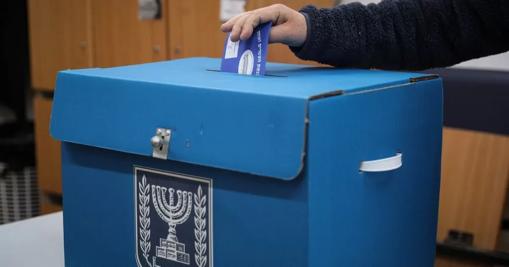 Mano introduciendo papeleta en urna de votación azul con emblema de Israel.