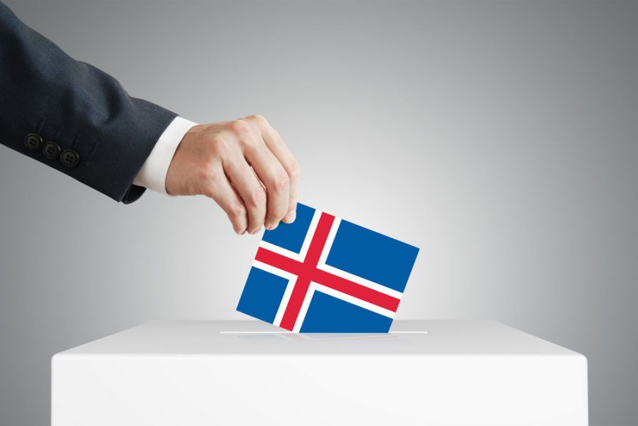 Mano introduciendo voto con bandera de Islandia en urna electoral.