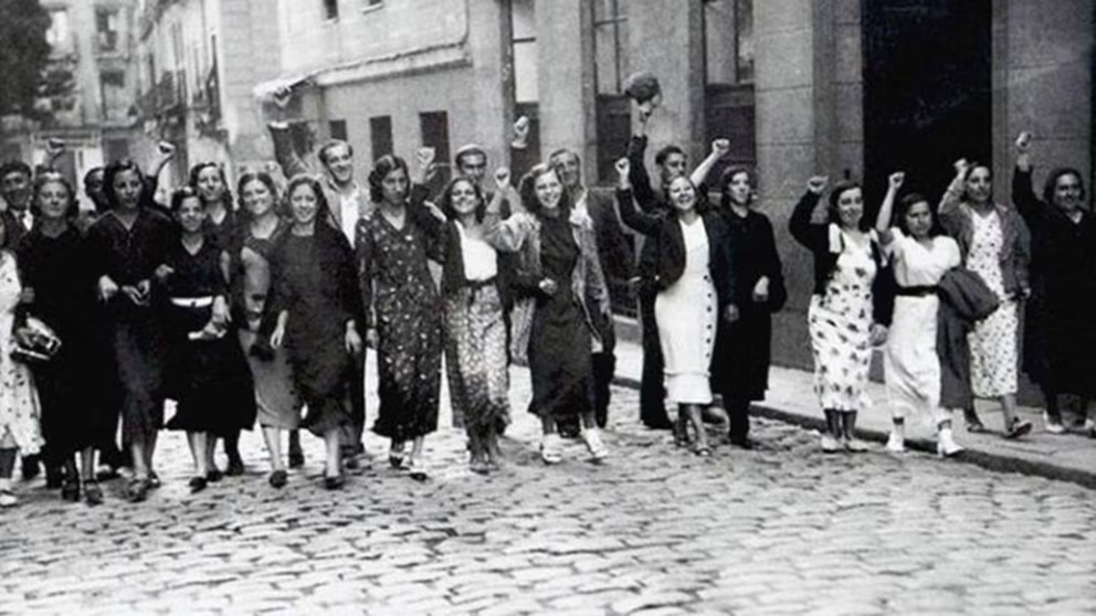 Mujeres con puños alzados marchan por calle empedrada.