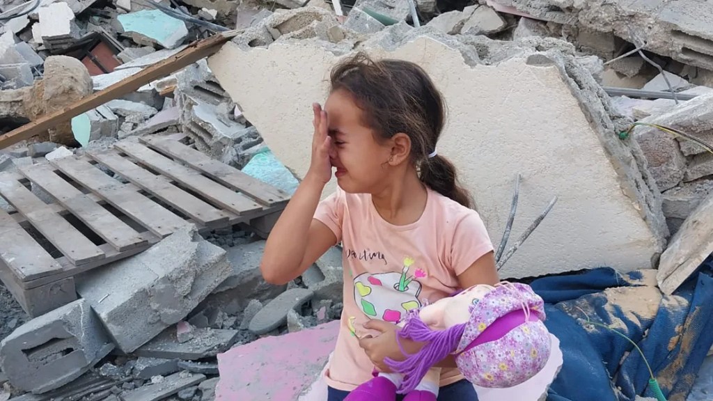 Niña llorando con muñeca entre escombros de destrucción.