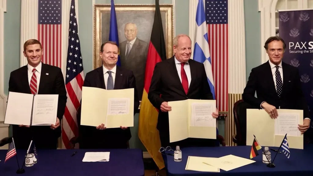 Cuatro hombres celebran un acuerdo multilateral entre EE. UU., Alemania y Grecia.