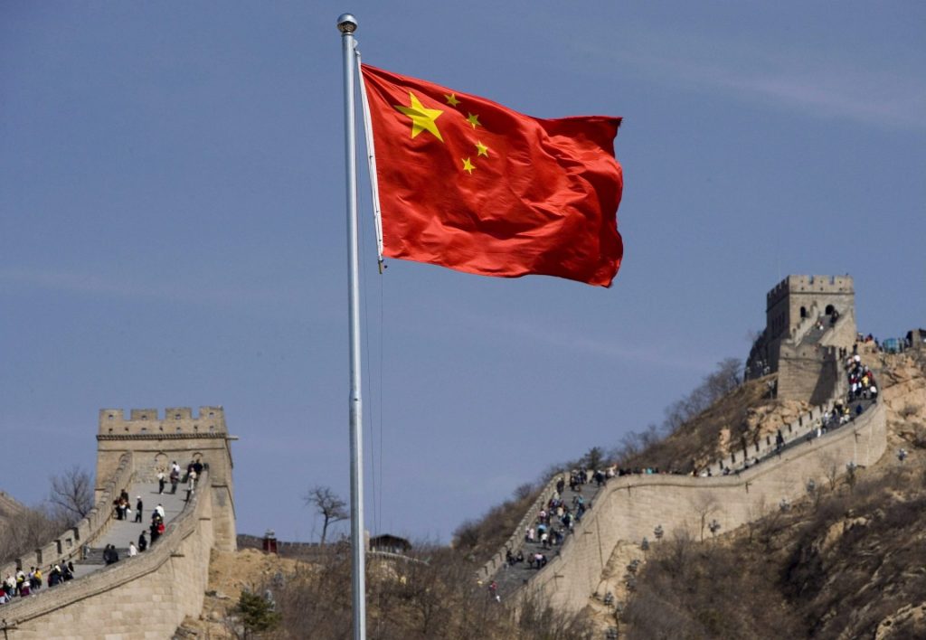 Bandera de China ondeando frente a la Gran Muralla con turistas.