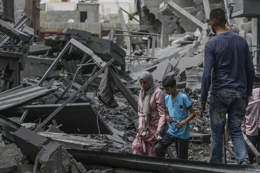 Familia camina entre escombros de edificios destruidos por conflicto.