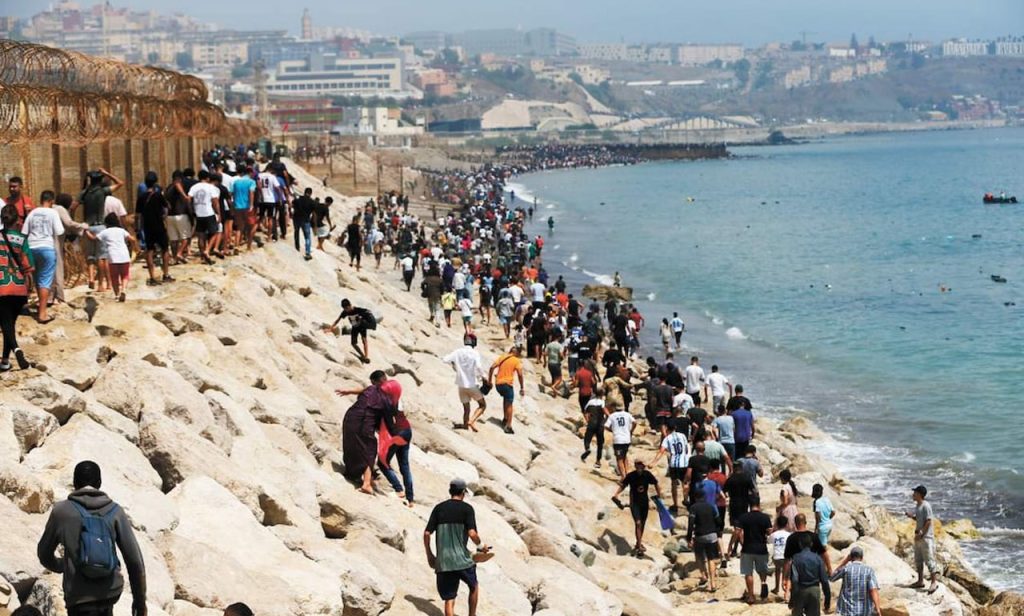 Gran multitud de personas avanzando por costa rocosa junto al mar.