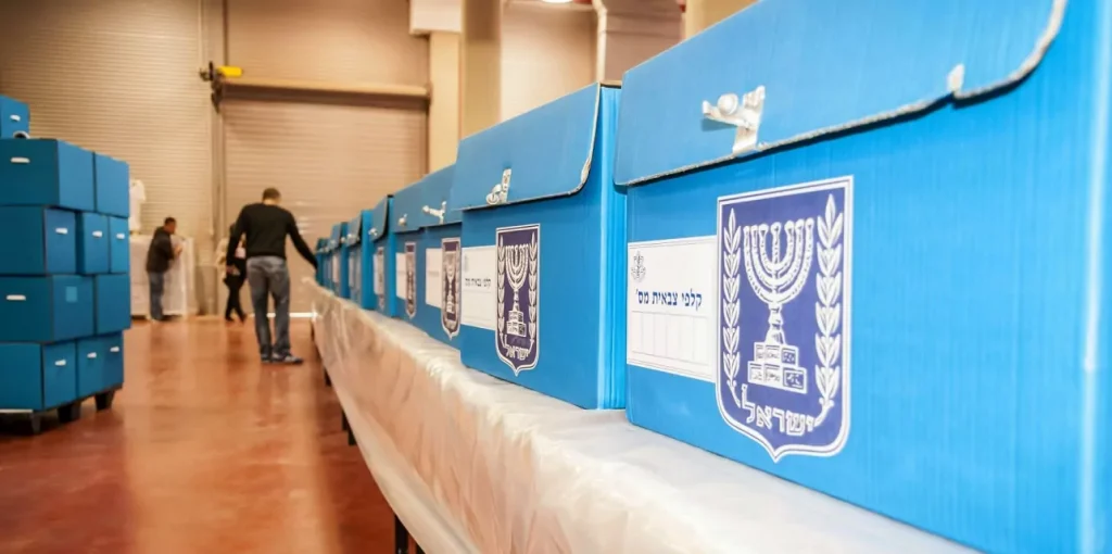 Cajas de votación israelíes azules en almacén con personas.