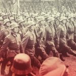 Soldados alemanes marchando en formación con uniformes y cascos históricos.