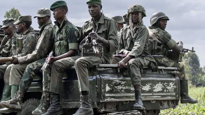 Soldados africanos armados sentados en la parte trasera de un camión militar.