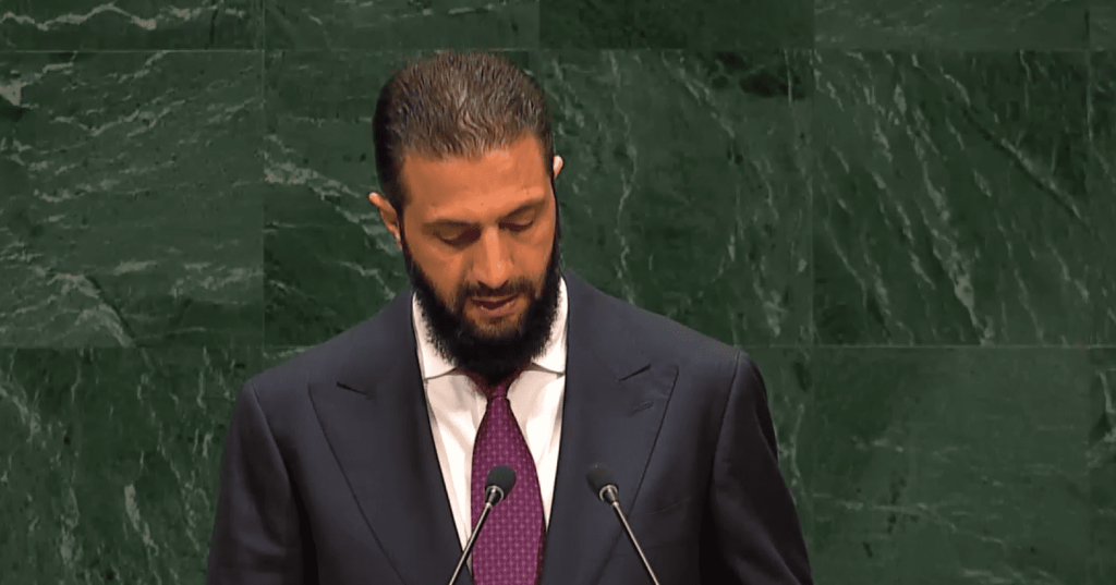 Hombre barbudo hablando en atril ONU, fondo mármol verde.