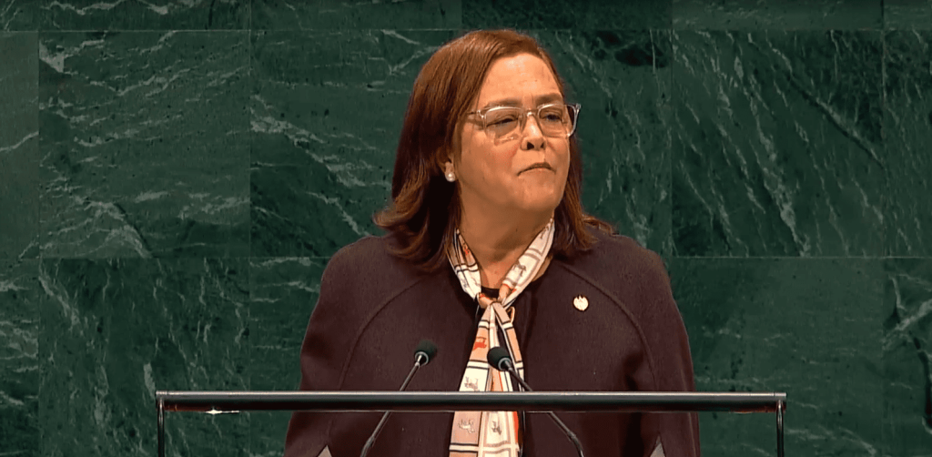 Mujer hablando en un podio con fondo de mármol verde.