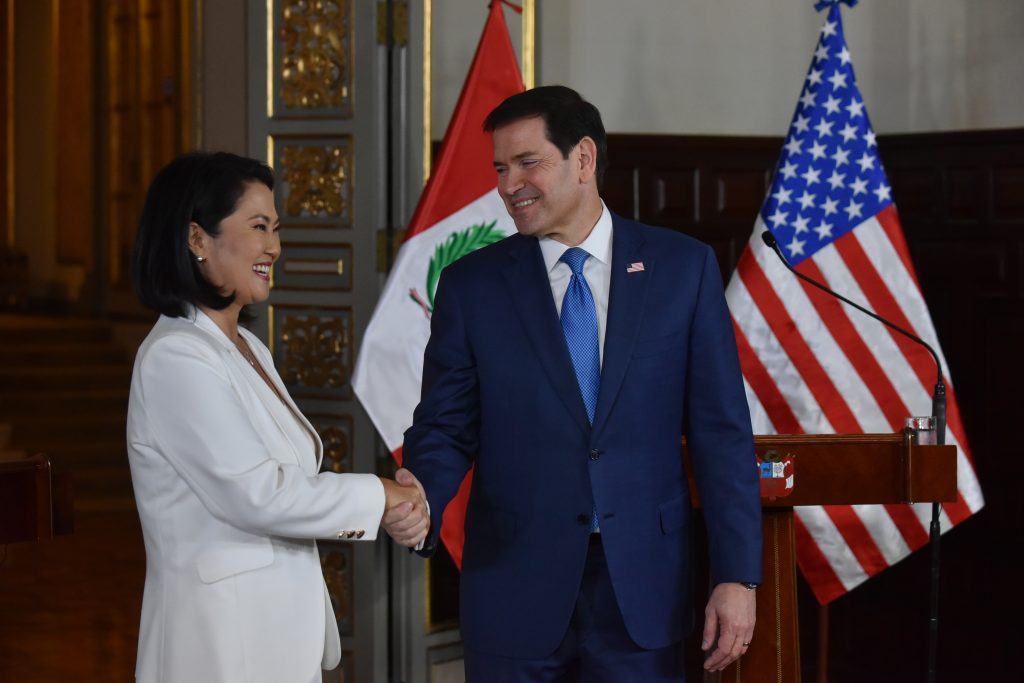 Dos personas sonrientes estrechándose la mano con banderas de Perú y EE. UU.