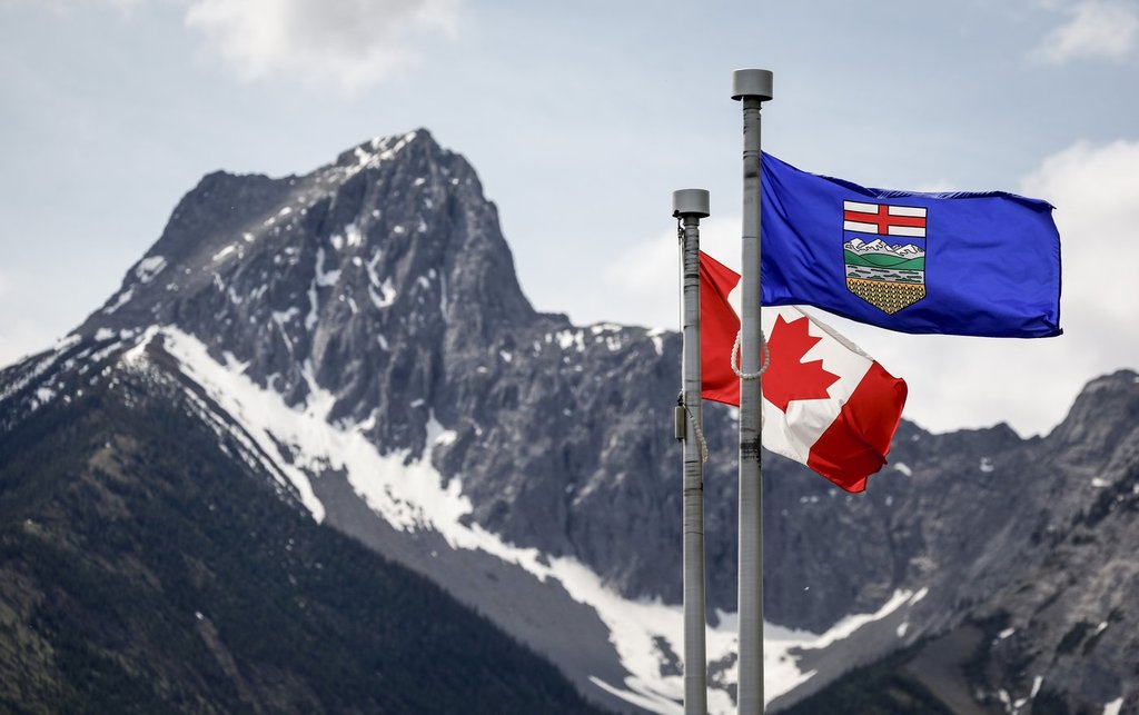 Banderas de Canadá y Alberta ondeando con montañas rocosas nevadas.