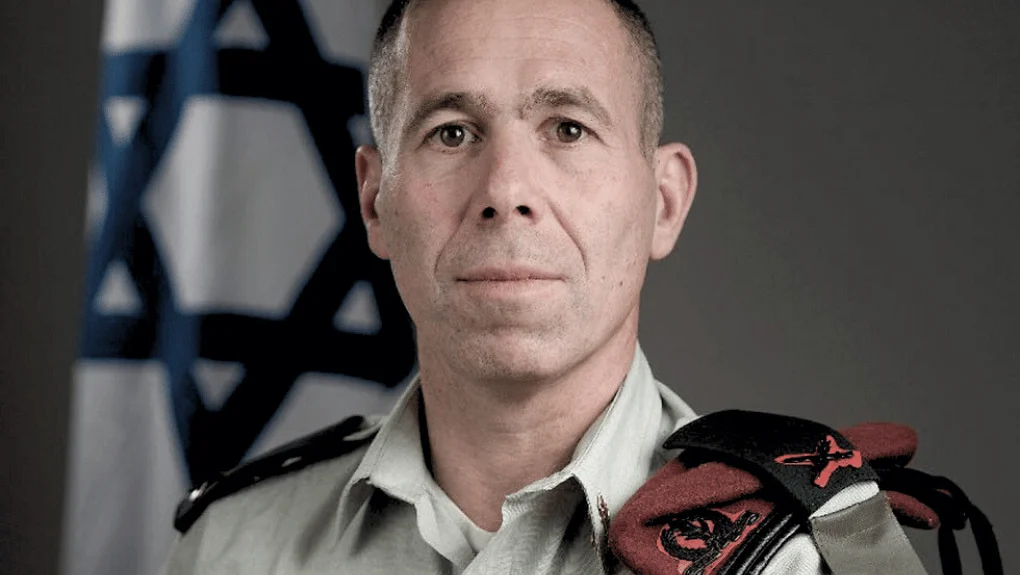 Oficial militar israelí con uniforme y boina roja, bandera de Israel.