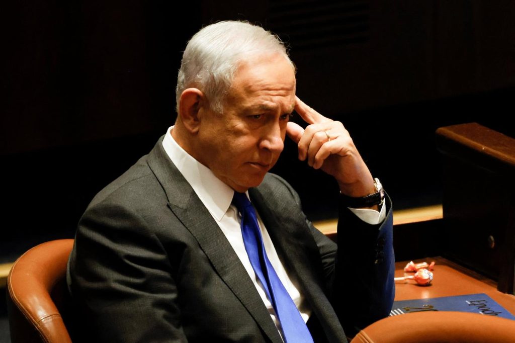 Benjamin Netanyahu pensativo en una reunión, tocándose la frente.