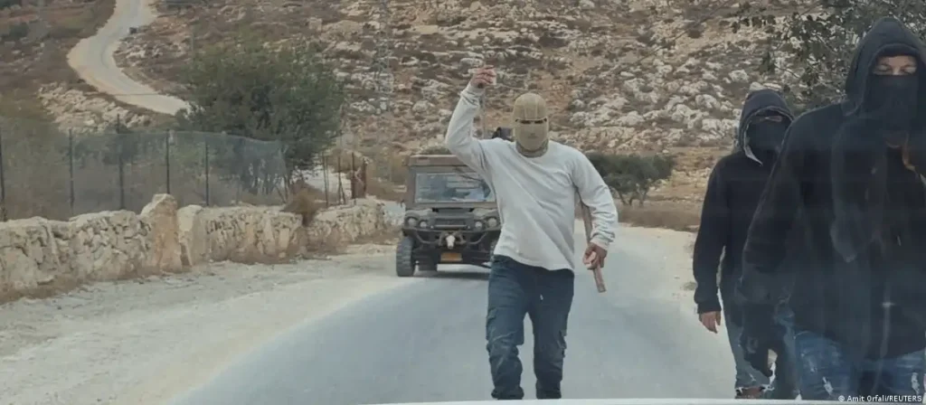 Hombres enmascarados, uno con palo, en carretera rural.