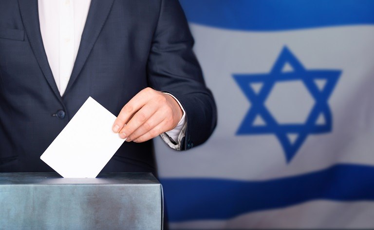 Persona votando en urna con bandera de Israel de fondo.