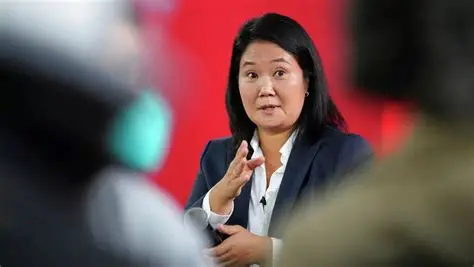 Mujer asiática hablando y gesticulando en evento profesional con fondo rojo.