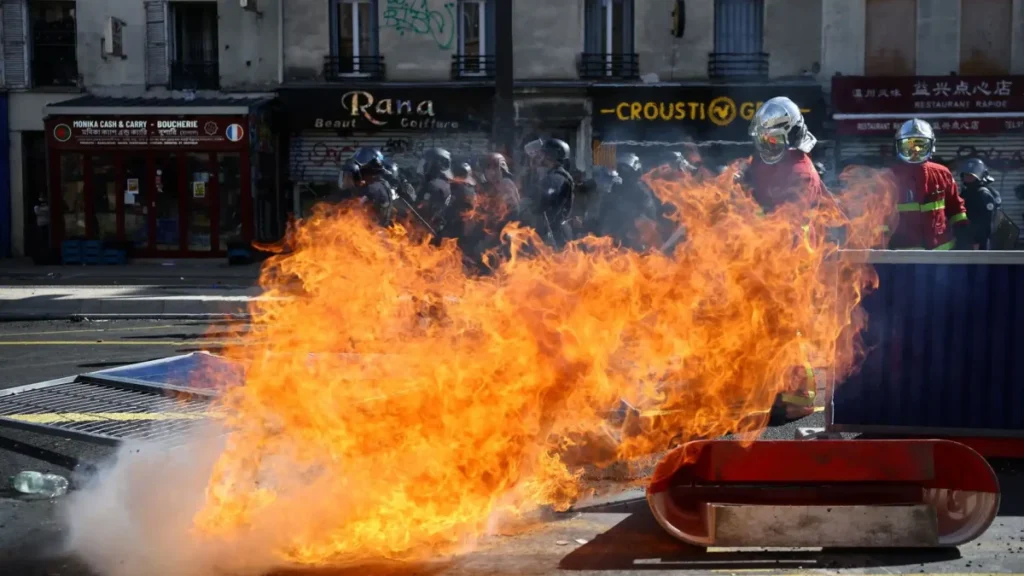 Gran fuego en calle durante protesta urbana con bomberos y policía.