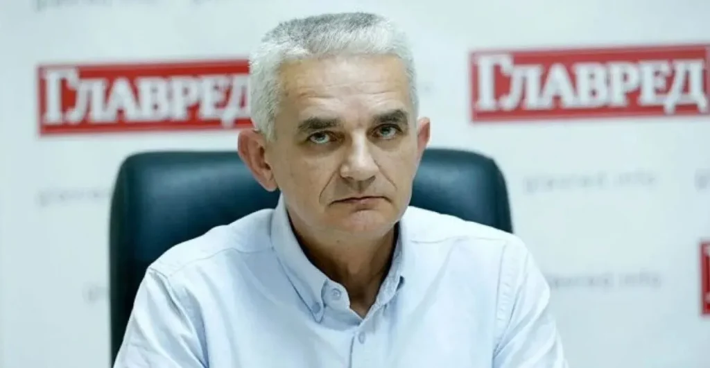 Hombre serio, pelo gris, camisa azul, frente a logo Glavred.