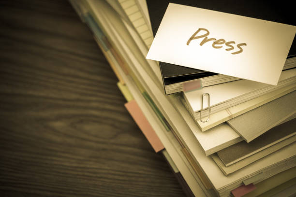 Pila de documentos y tarjeta 'Press' en un escritorio.