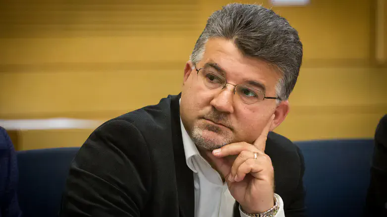 Hombre maduro con gafas, barba, traje oscuro, pensativo.